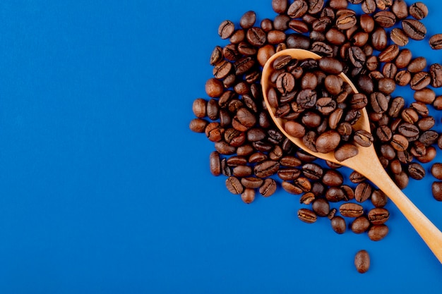 Coffee beans in a wooden spoon on coffee beans on blue background top view