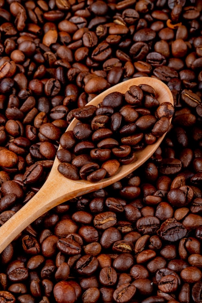 Free photo coffee beans in a wooden spoon on coffee beans top view