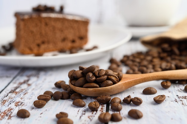 Coffee beans on wooden spoon on a white wood table.