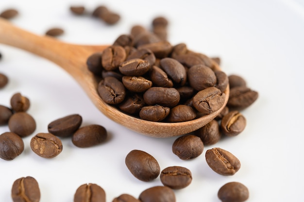 Coffee beans on wooden spoon on a white wood table.