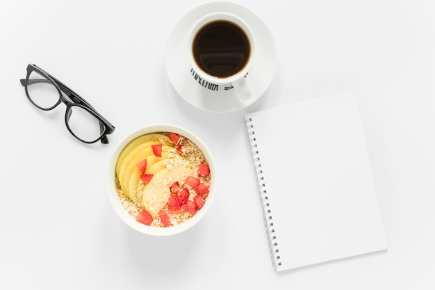 coffee and bowl with fruits and cereals beside notebook