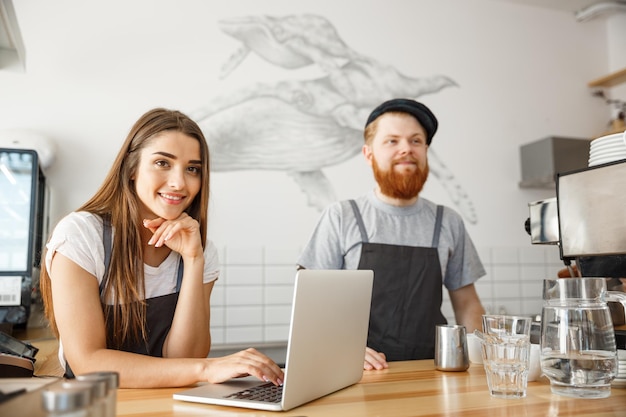 Coffee Business Concept Cheerful baristas looking at their laptop for online orders in modern coffee shop