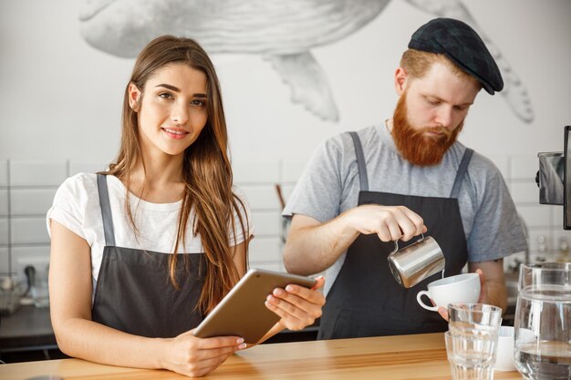 コーヒービジネスコンセプト現代のコーヒーショップでオンライン注文のためにタブレットを見ている陽気なバリスタ