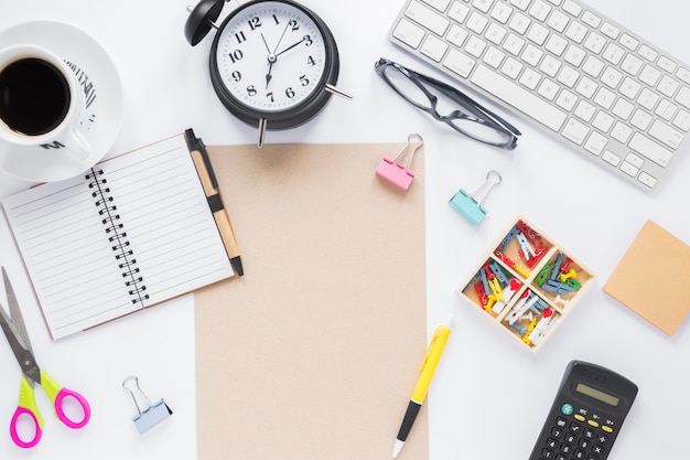 Coffee cup; alarm clock; keyboard and office supplies on white desk