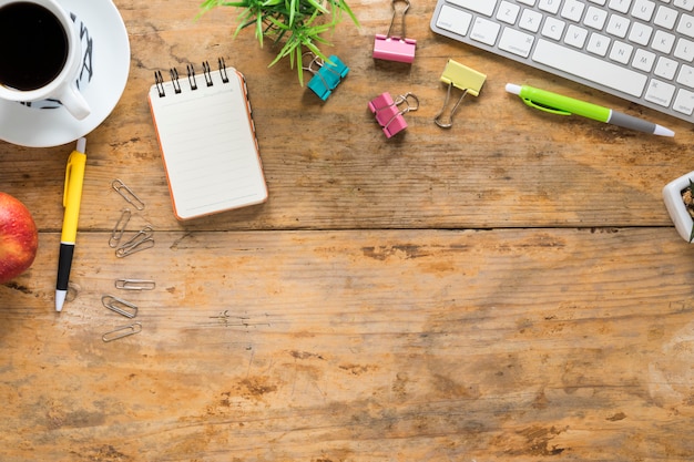 Coffee cup; apple; keyboard and office stationeries on wooden table