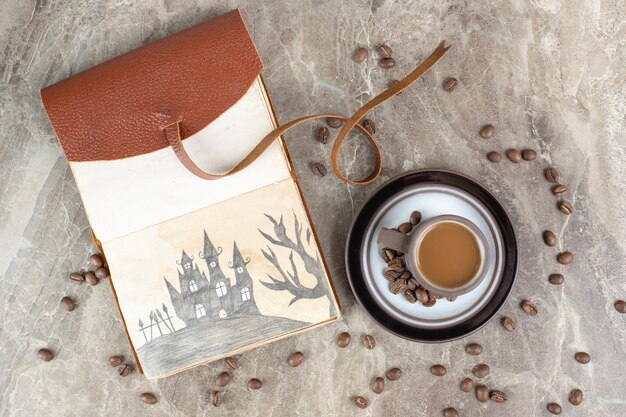 Coffee cup, beans and notebook on marble surface.