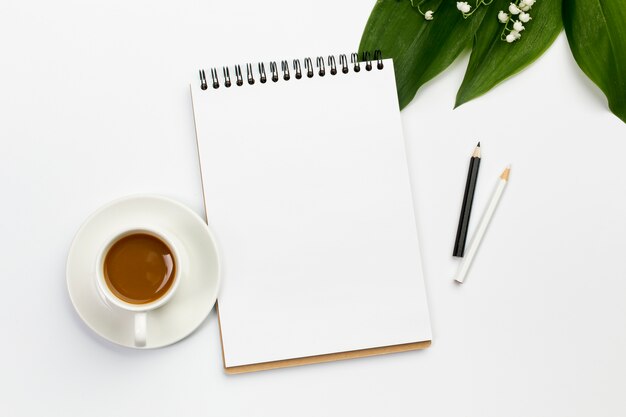 Coffee cup,blank spiral notepad and colored pencils with leaves and flower on office desk