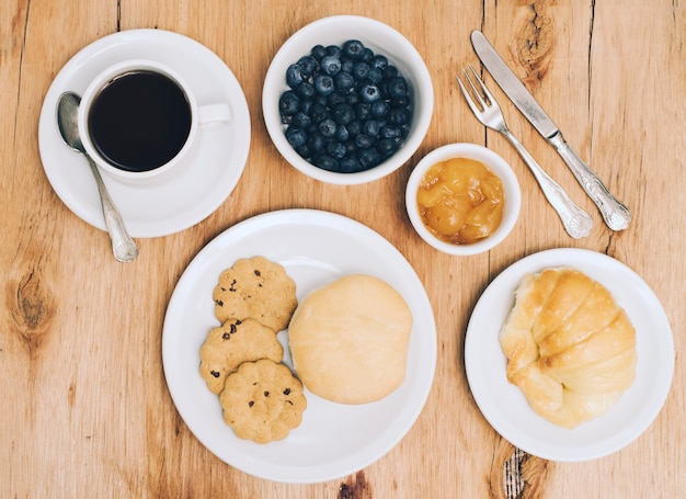 Coffee cup; blueberries; jam; bread; bun and cookies on table