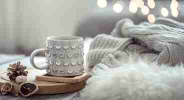 Free photo coffee cup over christmas lights bokeh in home on wooden table with sweater on a wall and decorations. holiday decoration, magic christmas