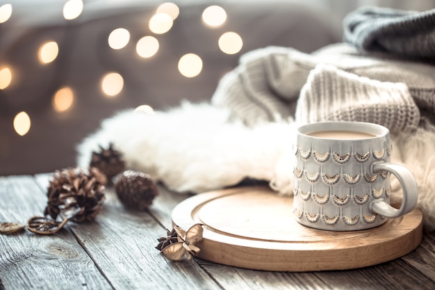 Чашка кофе над боке рождественских огней в доме на деревянном столе со свитером на стене и украшениями. Праздничное украшение