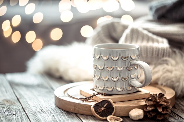 Coffee cup over Christmas lights bokeh in home on wooden table with sweater on a wall and decorations. Holiday decoration