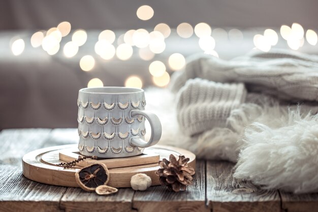 Coffee cup over Christmas lights bokeh in home on wooden table with sweater on a wall and decorations. Holiday decoration