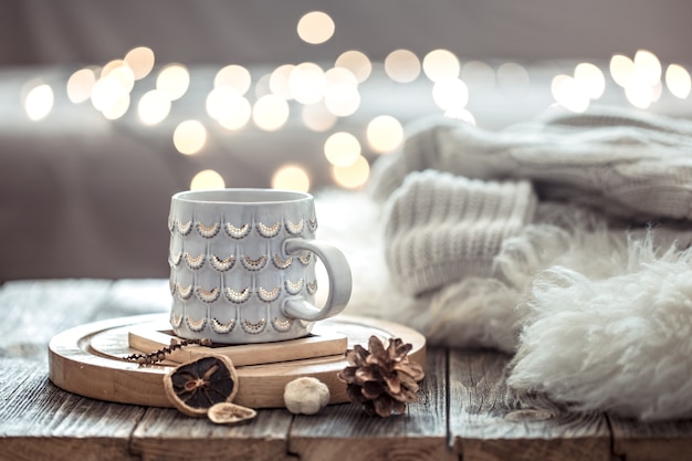 Coffee cup over Christmas lights bokeh in home on wooden table with sweater on a wall and decorations. Holiday decoration