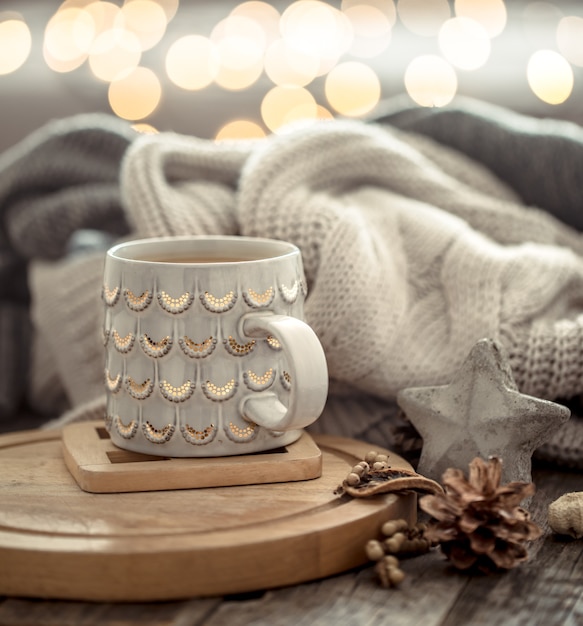 Coffee cup over Christmas lights bokeh in home on wooden table with sweater on a wall and decorations. Holiday decoration