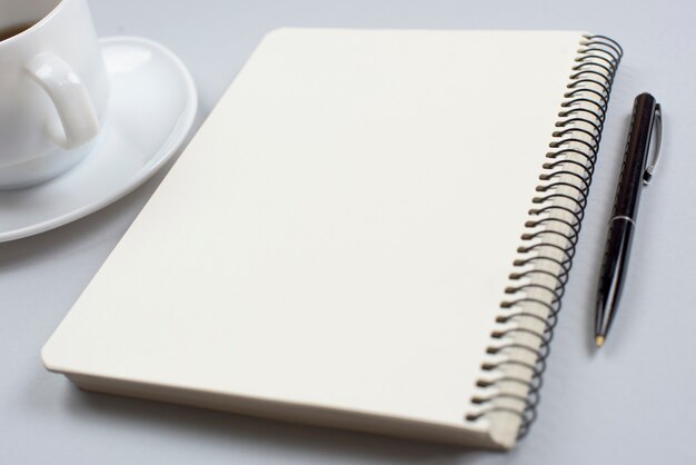 Coffee cup; closed spiral notepad and pen on gray background