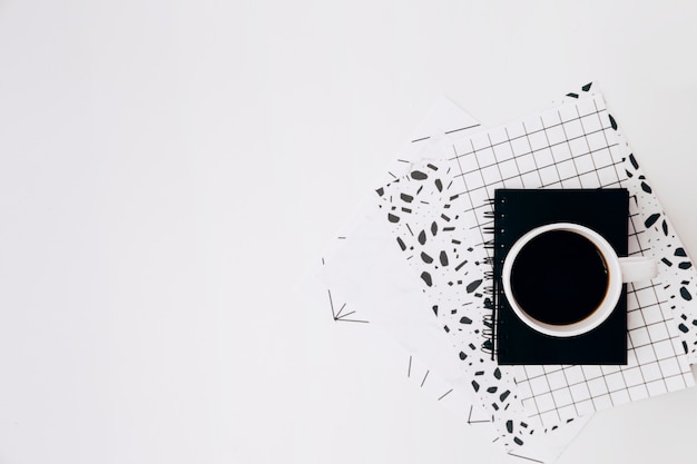 Coffee cup and diary on design papers against white backdrop