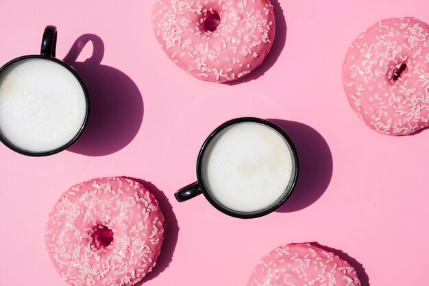 Кофейная чашка и пончики на розовом фоне