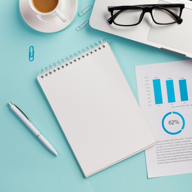 Coffee cup,eyeglasses,laptop,eyeglasses,data paper,pen and blank spiral notepad