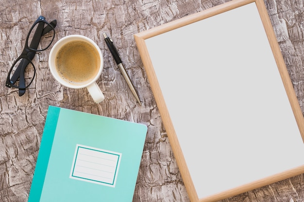 Coffee cup; eyeglasses; pen; picture frame and notebook on textured background