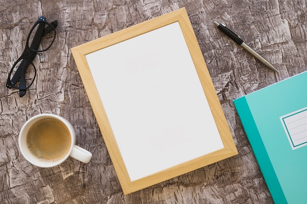 Coffee cup; eyeglasses; picture frame; pen and notebook on textured background