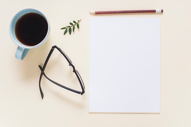 Coffee cup; eyeglasses; twig; pencil and blank white page on beige backdrop