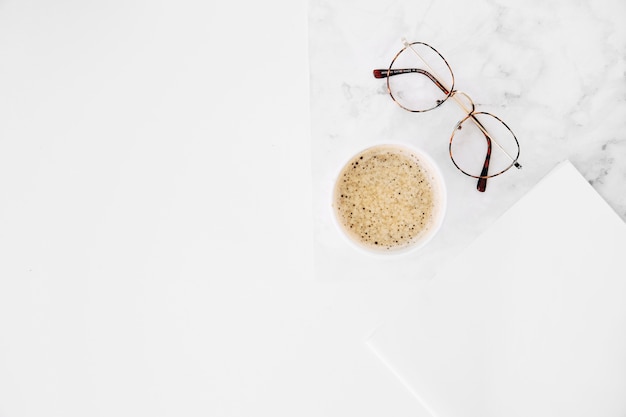 Coffee cup and eyeglasses with white paper on white background