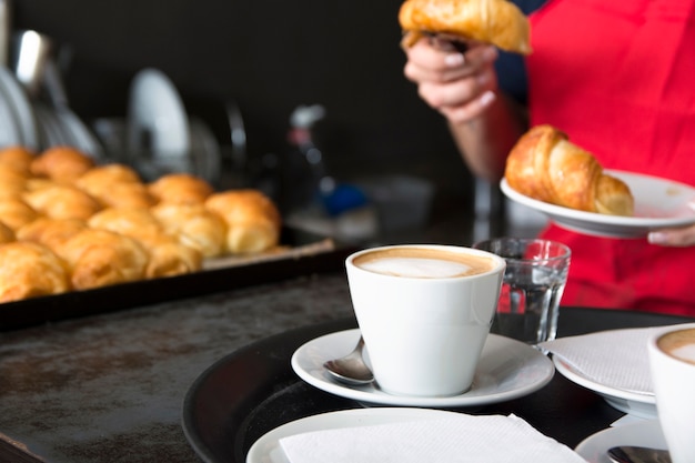 Tazza di caffè davanti alla cameriera mettendo croissant nel piatto