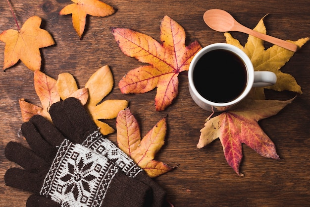 Coffee cup and gloves on autumn leaves background