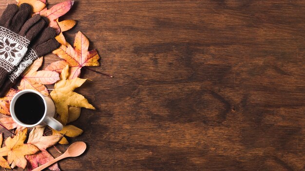 Coffee cup and gloves on autumn leaves copy space