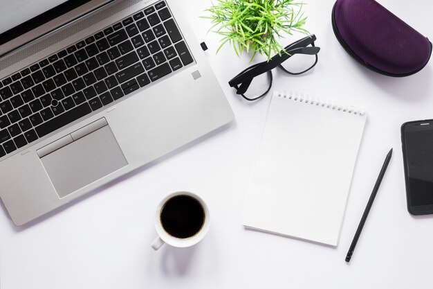 Coffee cup; laptop; eyeglasses; pencil and spiral notepad with pencil on white backdrop