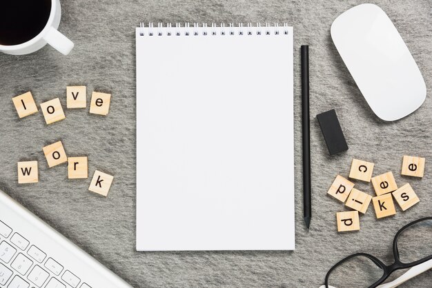 Coffee cup; love work blocks; keyboard; mouse; spiral notepad; pencil and eraser on gray backdrop