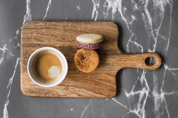 Free photo coffee cup and macaroons on chopping board over the marble backdrop