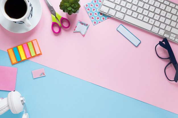 Coffee cup; office stationeries; keyboard and headphone on pink and blue background