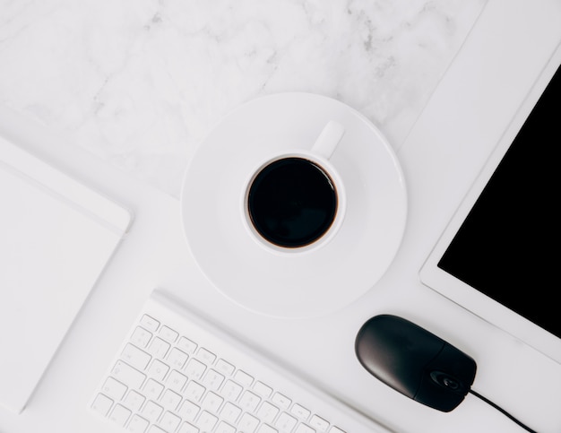 Coffee cup and saucer with mouse; coffee cup; digital tablet; diary and keyboard on white desk