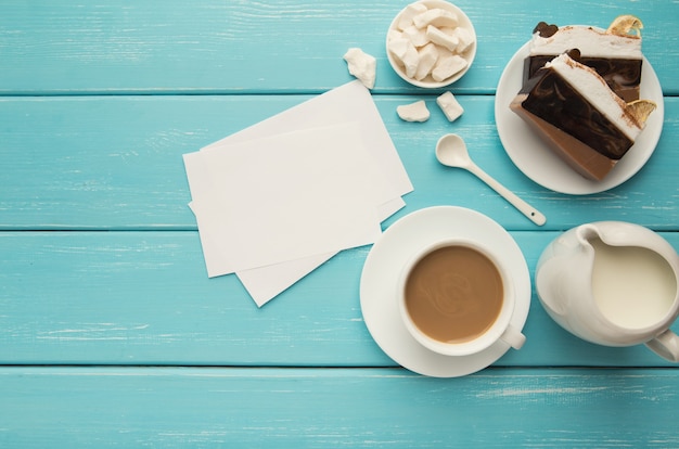 上​から​青い​素朴な​テーブル​の​上​の​ケーキ​の​部分​と​紙​の​メモ​と​コーヒー​カップ​。​居心地​の​良い​おいしい​朝食​の​上面図​、​コピー​スペース