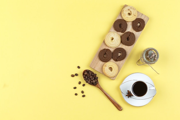 Coffee in cup with coffee beans, biscuits, dried herbs on yellow background