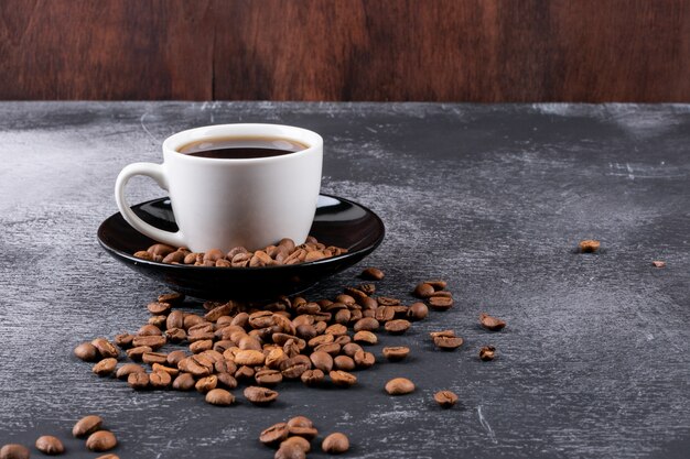 暗いテーブルの上のコーヒー豆とコーヒーカップ