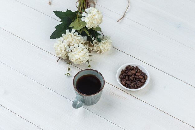 Coffee in a cup with coffee beans, flowers high angle view on a wooden background