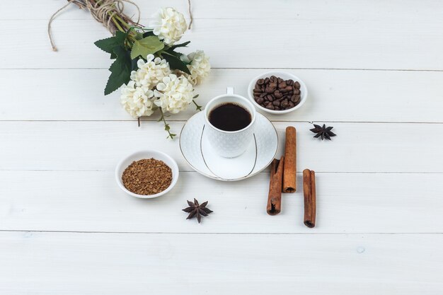 Coffee in a cup with coffee beans, spices, flowers, grinded coffee high angle view on a wooden background