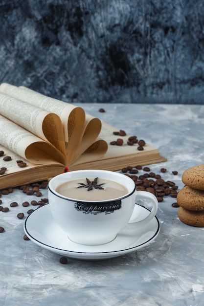 Coffee in a cup with cookies, coffee beans, book high angle view on a grungy plaster background