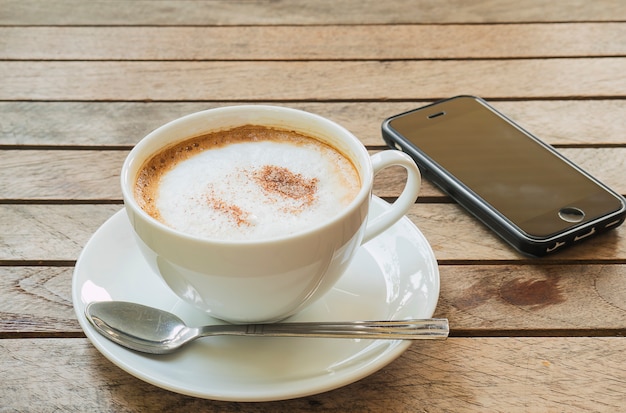 Coffee cup with mobile phone over brown plank wood table