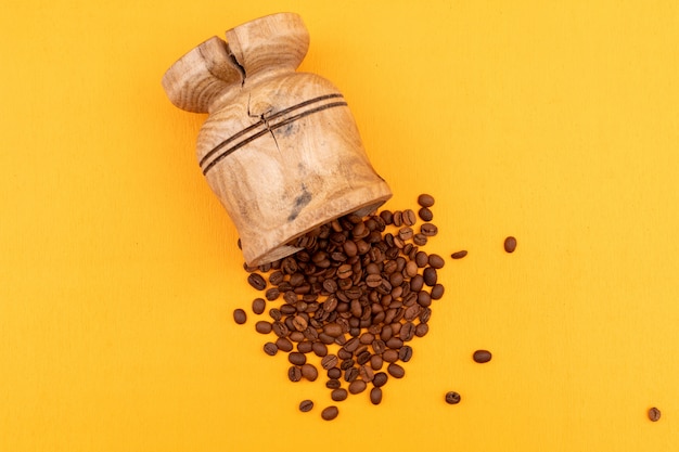 Foto gratuita tazza di caffè con i chicchi di caffè marroni arrostiti su superficie gialla