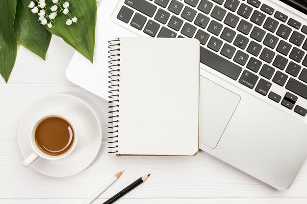 Coffee cup with spiral notepad on laptop with colored pencils on office wooden desk