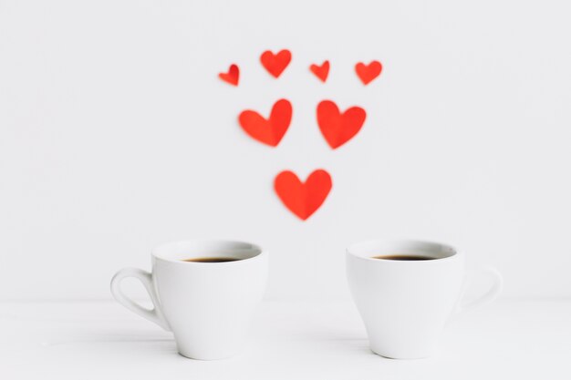 Coffee cups near paper hearts composition