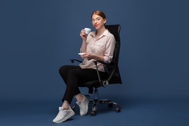 Free photo coffee drinking. young woman in casual wear on blue studio wall