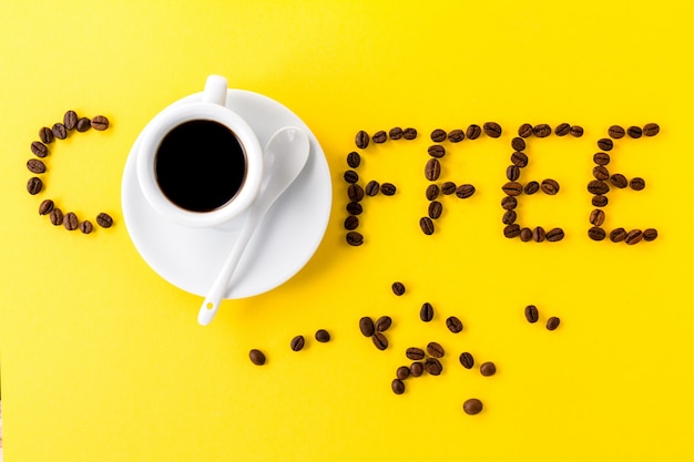 Free photo coffee espresso in small white ceramic cup with coffee beans and word coffee