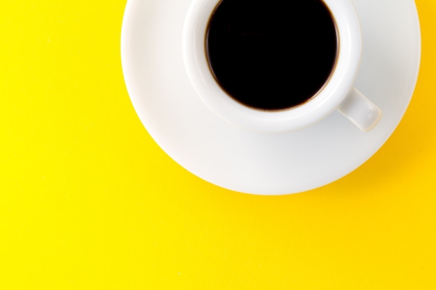 小さなエスプレッソ、小さな白いセラミックカップで、黄色の活気のある背景に。ミニマルフードモーニングエネルギーコンセプト。