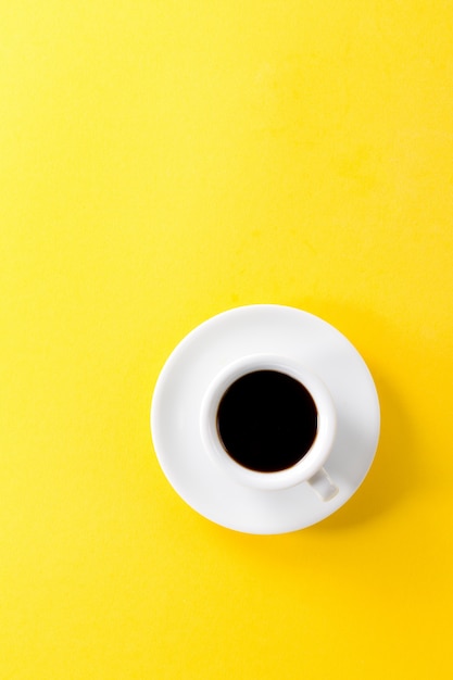コーヒーのエスプレッソは、小さな白いセラミックのカップで黄色の活気のある背景に