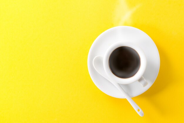 Coffee espresso in small white ceramic hot steam cup on yellow vibrant background. Minimalism Food Morning Energy Concept.