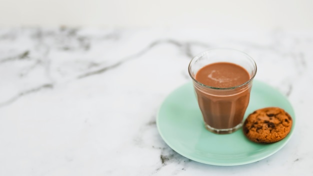 Coffee glass and single cookies on turquoise plate over the marble backdrop